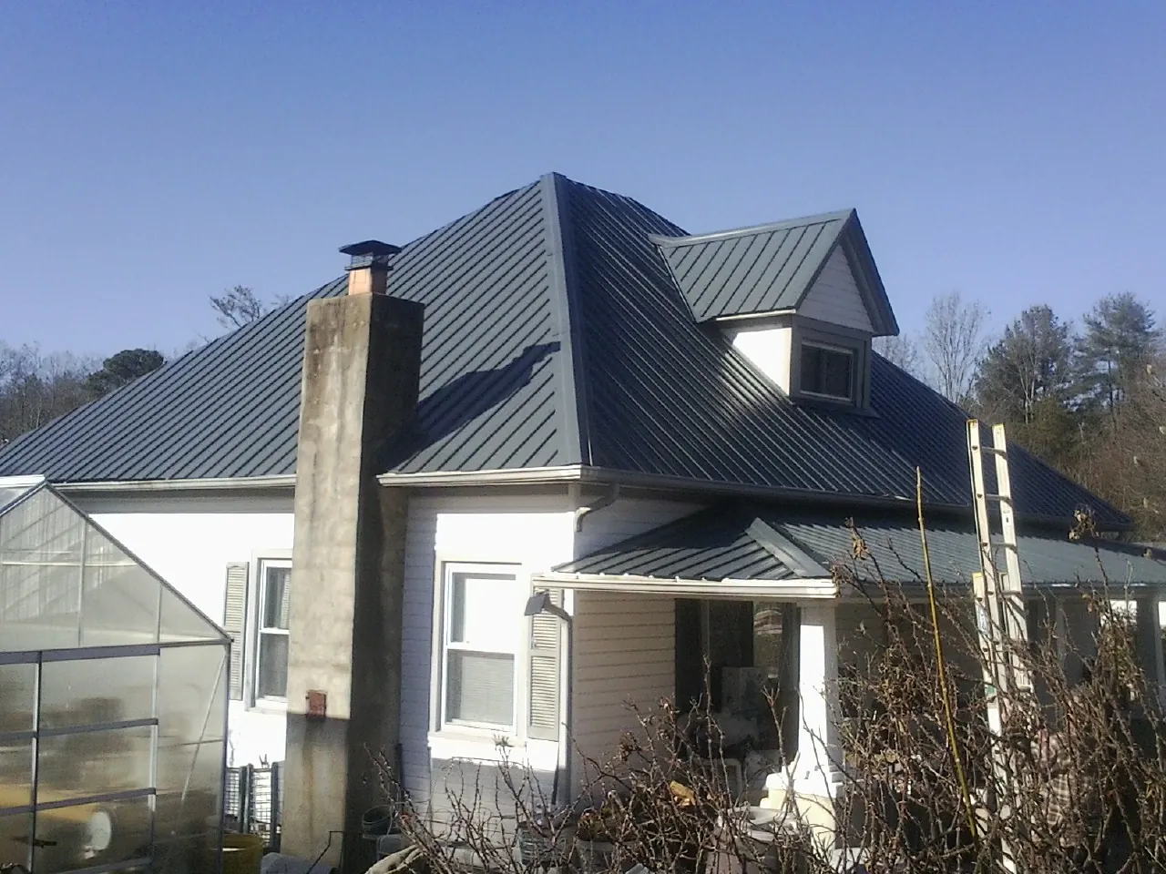 Dark blue standing seam metal roof on a white farmhouse with dormer — Slate & Tile Roof Repair by Roofing Brothers in Panacea
