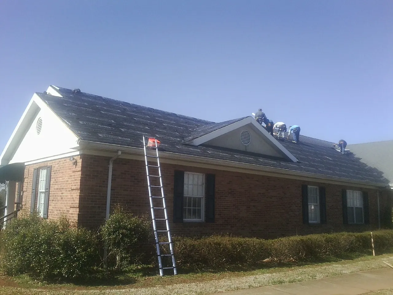Crew tearing shingles off a brick ranch roof with a ladder set — Metal Roof Repair work by our crew in Panacea