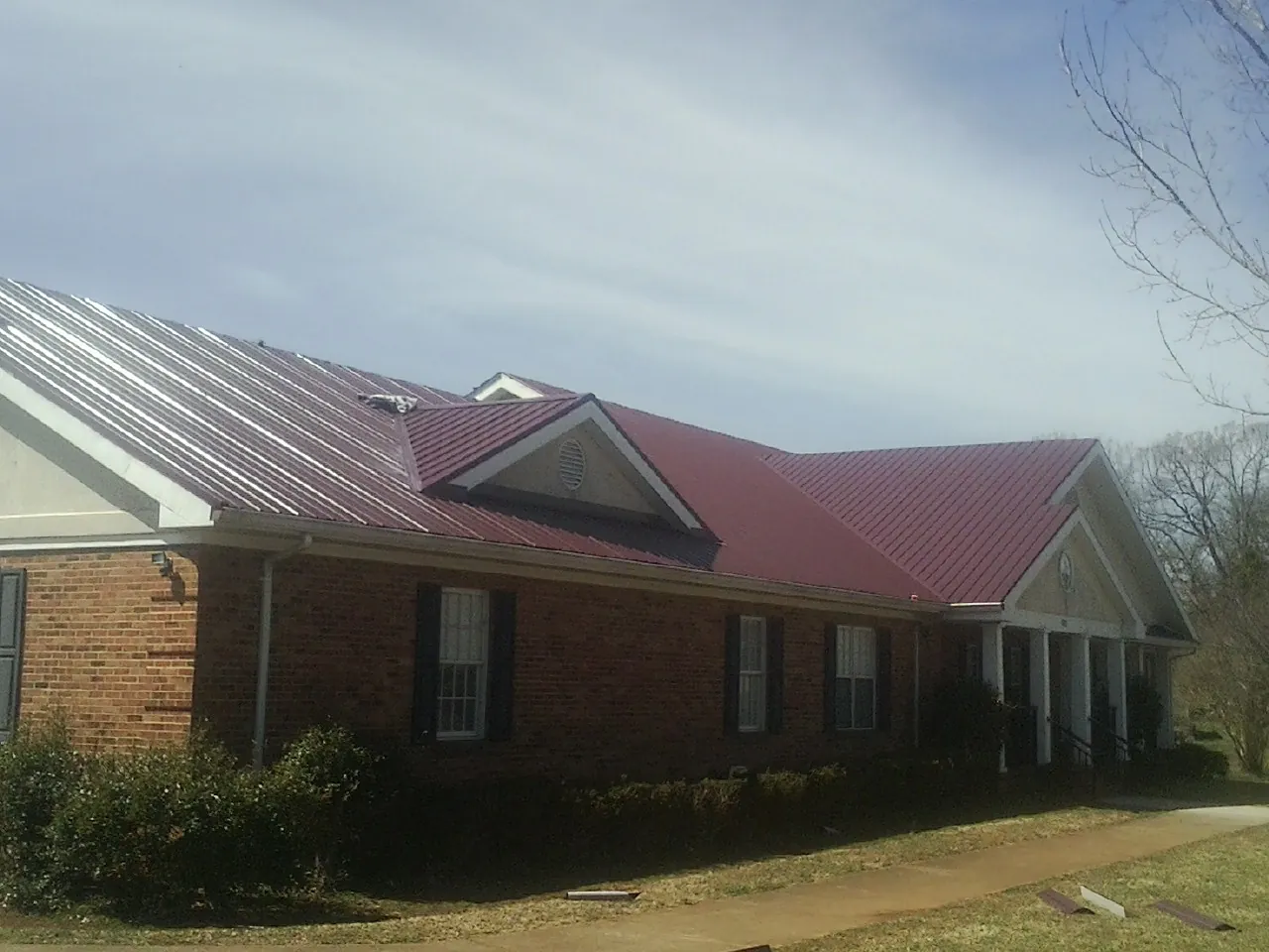 Red metal roof with gabled entries on a long brick building, from a Hail Damage Roof Repair job in Panacea