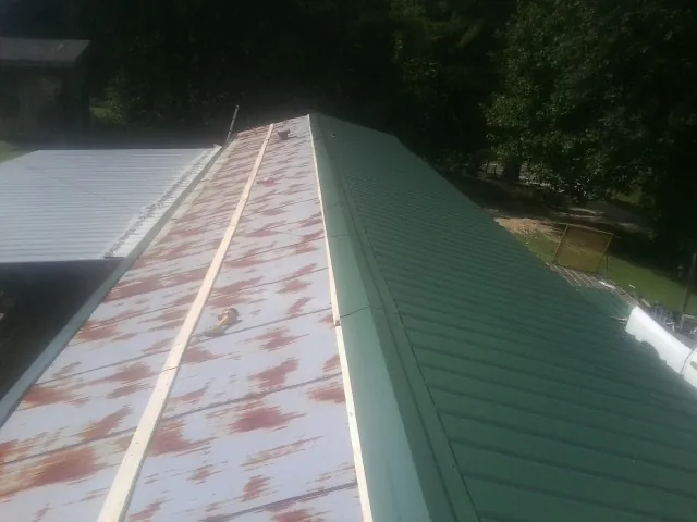 Old rusted panels beside newly installed green metal roofing — Wind Damage Roof Repair by Roofing Brothers in Panacea