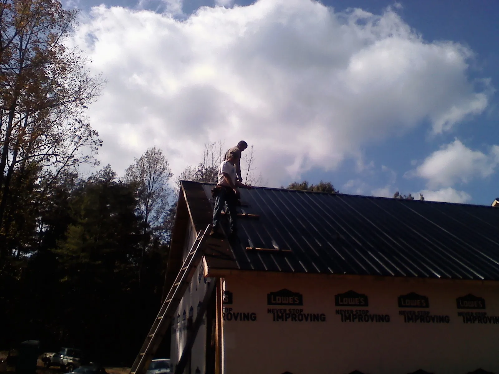 Roofer fastening dark metal panels high against a cloudy sky, from a Roof Inspection job in Panacea